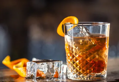 Glass of light rum with an orange twist and ice on a wooden bar.